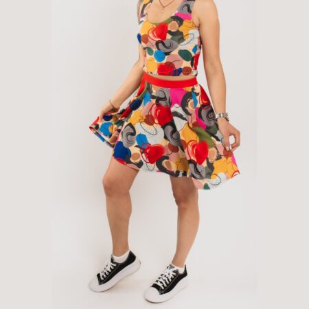 Saules piegriezuma svārki ar košu un abstraktu dizainu komplektā ar tāda paša dizaina sieviešu īso topu, demonstrē modele