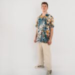 Stilīgs vīrietis, kurš pozē baltā fonā, valkājot brīva stila kreklu “Melvin” ar abstraktu, daudzkrāsainu apdruku. Krekls ir kombinēts ar gaišām biksēm, radot atpūtai piemērotu stilu.