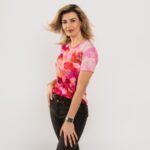 rozā pamatkrāsas t-krekls ar maigām krāsu pārejām no rozā uz viegli violetu, stilizētas sakuras dizainā, sieviete no kreisā sāna